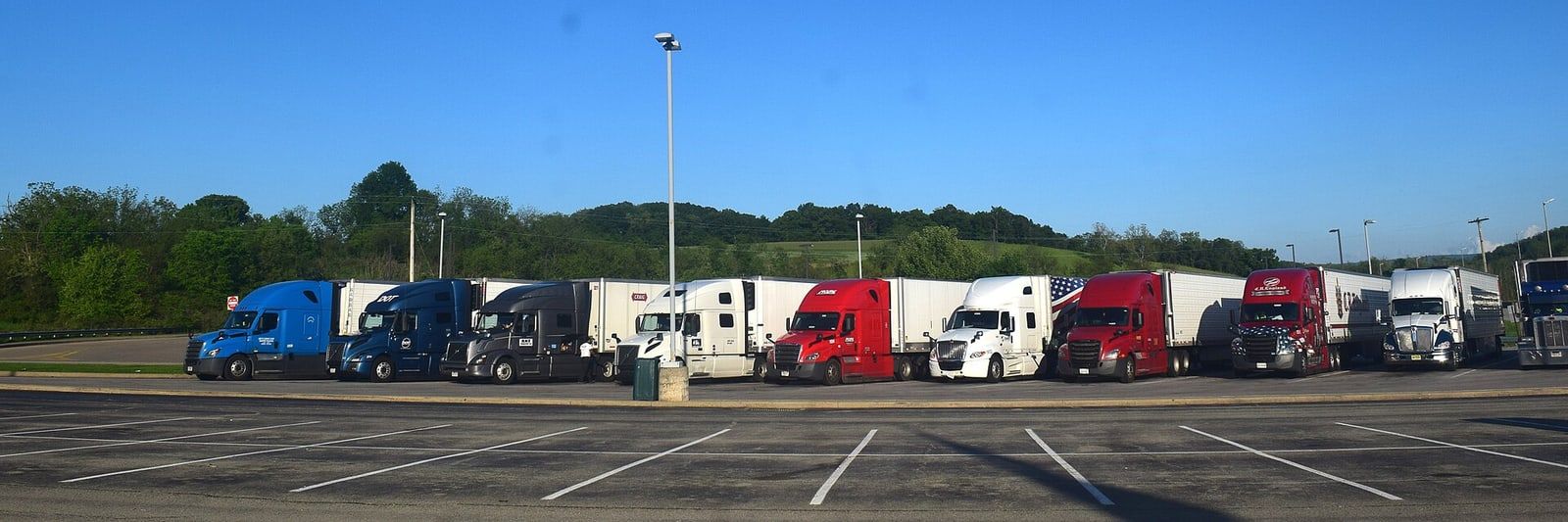 A row of semi trucks with trailers parked at a truck stop under a clear sky